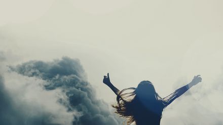 Femme levant les bras au ciel sur fond de nuages