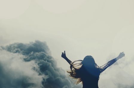 Femme levant les bras au ciel sur fond de nuages