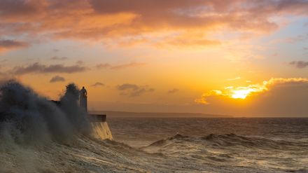 Phare au milieu d'une vague sur fond de lever de soleil