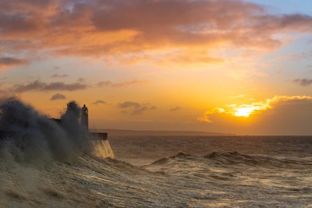 Phare au milieu d'une vague sur fond de lever de soleil