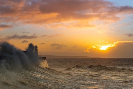 Phare au milieu d'une vague sur fond de lever de soleil