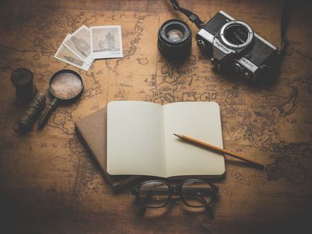 Carnet aux pages blanches avec un crayon de bois, entouré d'une loupe, d'un appareil photo ancien et de divers objet, posés sur une carte ancienne du monde