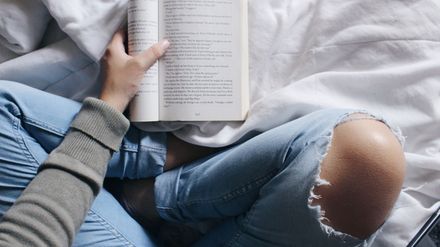 Personne en train de lire un livre, vue de dessus sur son lit, croisant les genoux