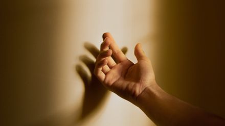 Main masculine ouverte projettant son ombre contre un mur ensoleillé sur lequel est est posée