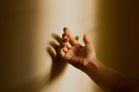 Main masculine ouverte projettant son ombre contre un mur ensoleillé sur lequel est est posée