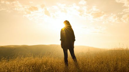Silhouette d'une femme devant un éclat de soleil, dans un champ sur une colline