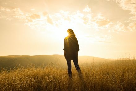 Silhouette d'une femme devant un éclat de soleil, dans un champ sur une colline