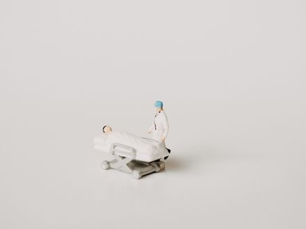 2 petits jouets représentant un chirurgien et son patient alité, sur fond blanc