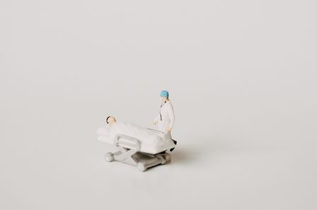2 petits jouets représentant un chirurgien et son patient alité, sur fond blanc