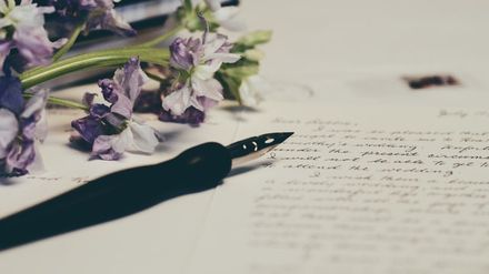 Stylo plume sur une lettre manuscrite bordée de fleurs violettes