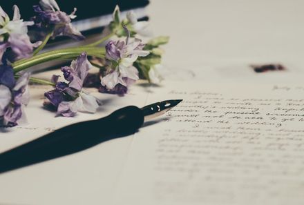 Stylo plume sur une lettre manuscrite bordée de fleurs violettes