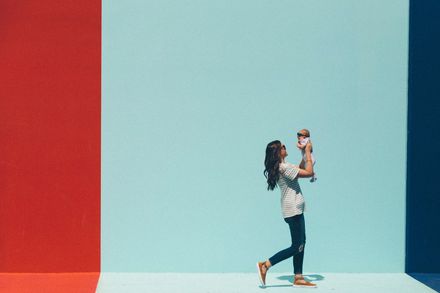 Maman tenant son bébé à bout de bras, devant un mur coloré bleu et rouge