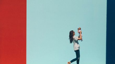 Maman tenant son bébé à bout de bras, devant un mur coloré bleu et rouge