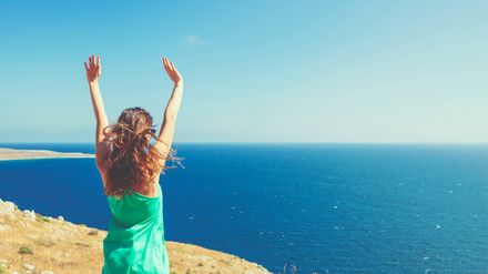 Femme les bras levées devant la mer, le vent dans les cheveux