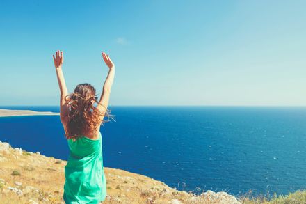 Femme les bras levées devant la mer, le vent dans les cheveux
