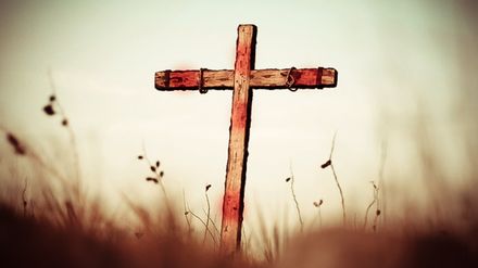 Croix en bois vide avec des traces de sang dans un champ d'herbes hautes