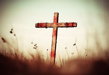 Croix en bois vide avec des traces de sang dans un champ d'herbes hautes
