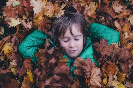 Jeune garçon en blouson vert se reposant les yeux fermés sur un tapis de feuilles mortes