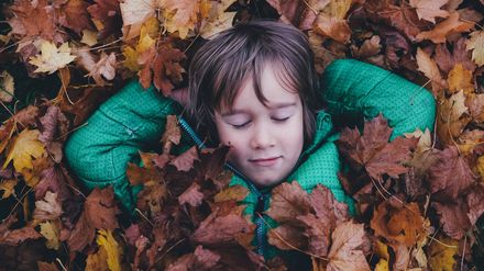 Jeune garçon en blouson vert se reposant les yeux fermés sur un tapis de feuilles mortes