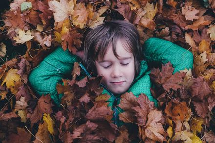 Jeune garçon en blouson vert se reposant les yeux fermés sur un tapis de feuilles mortes