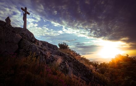 Croix en bois avec le corps de Jésus suspendu en haut d'une colline sur fond de lever de soleil