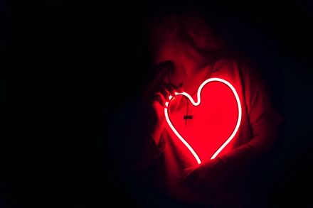 Femme tenant un néon rouge en forme de coeur sur sa poitrine
