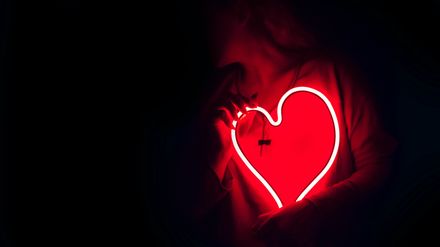 Femme tenant un néon rouge en forme de coeur sur sa poitrine