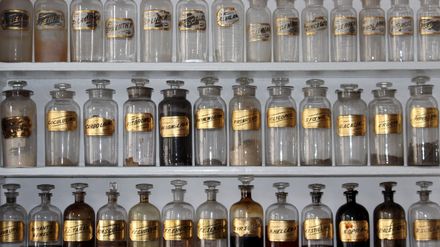 Etagères de récipients transparents anciens avec des étiquettes dorées contenant des parfums
