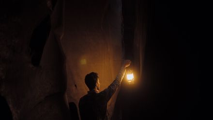 Jeune homme marchant dans une caverne sombre tenant une lampe ancienne allumée dans la main