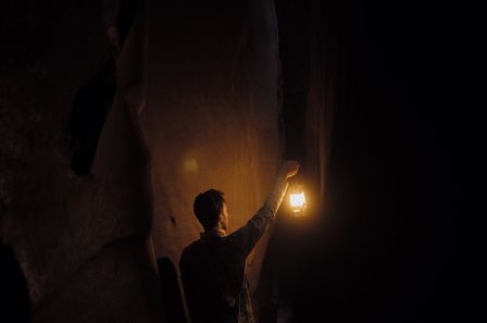 Jeune homme marchant dans une caverne sombre tenant une lampe ancienne allumée dans la main