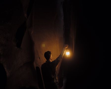 Jeune homme marchant dans une caverne sombre tenant une lampe ancienne allumée dans la main