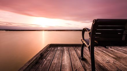 Banc sur une jetée en bois devant un lac calme sur lever de soleil aux couleurs rosées