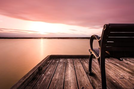 Banc sur une jetée en bois devant un lac calme sur lever de soleil aux couleurs rosées