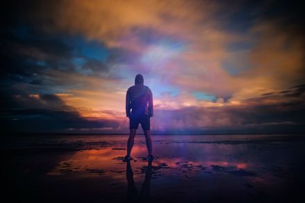 Un homme de dos se tient debout déterminé devant la mer au lever du soleil