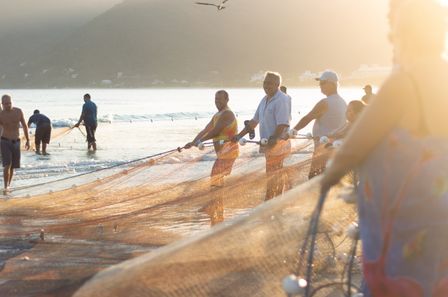 Groupe d'hommes tenant un filet de pêche sur une plage dans une atmosphère de soleil rasant