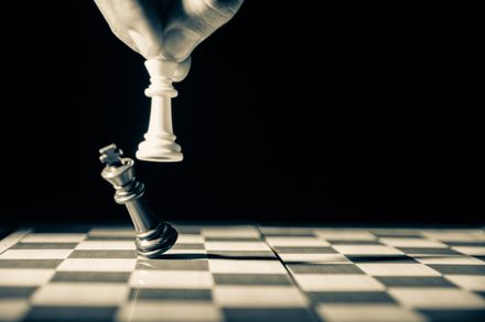 Photo en noir et blanc de la main d'un joueur d'échecs dont le roi blanc renverse le roi noir