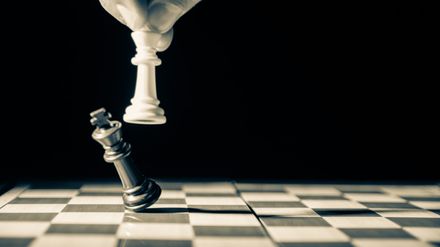 Photo en noir et blanc de la main d'un joueur d'échecs dont le roi blanc renverse le roi noir