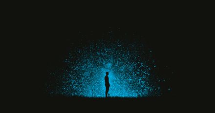 Silhouette d'un homme debout dans l'obscurité devant un panache de lumière bleue