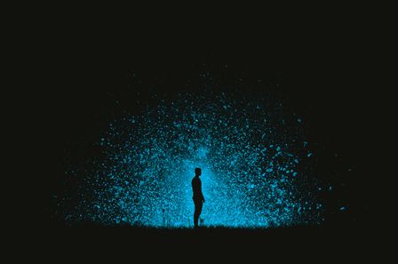 Silhouette d'un homme debout dans l'obscurité devant un panache de lumière bleue