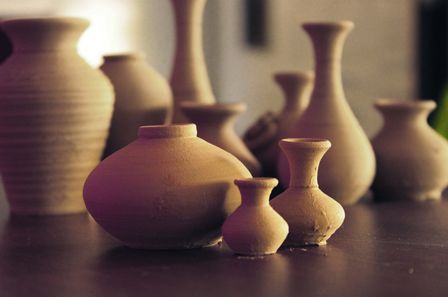 Ensemble de vases d'argiles de tailles et formes diverses venant d'être façonnés, pas encore secs, posés sur une table de bois