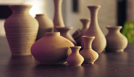 Ensemble de vases d'argiles de tailles et formes diverses venant d'être façonnés, pas encore secs, posés sur une table de bois