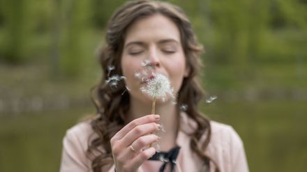 Femme soufflant une fleur de pissenlit
