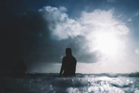Personne marchant au milieu de la mer sur un ciel d'orage percé d'un rayon de soleil
