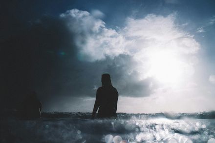 Personne marchant au milieu de la mer sur un ciel d'orage percé d'un rayon de soleil