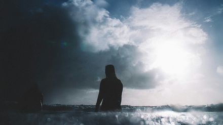 Personne marchant au milieu de la mer sur un ciel d'orage percé d'un rayon de soleil